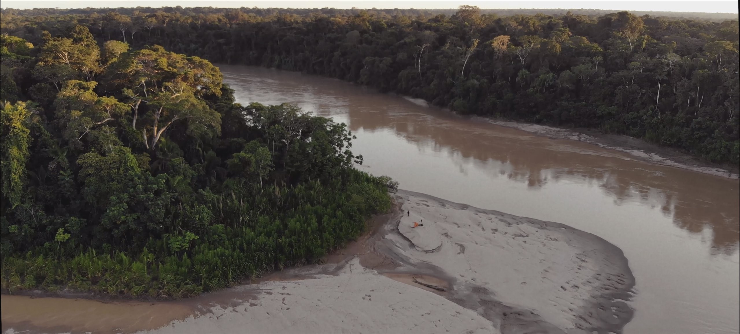 This image shows the Las Piedras river in the Amazon and you can see Paul Rosolie walking on sand with an orange tent.jpg